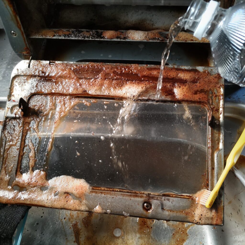 トースター前扉をこすった後、ペットボトルの水で洗剤を流す様子